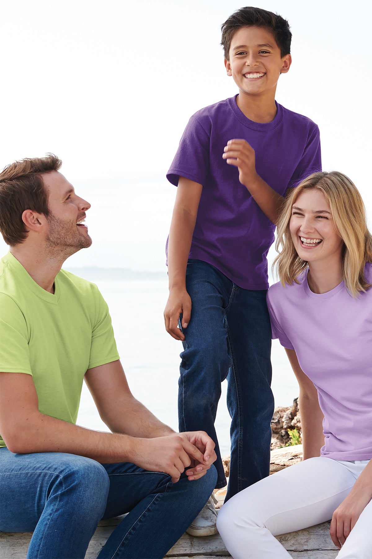 Three people sitting together on a wooden dock by the water, smiling.