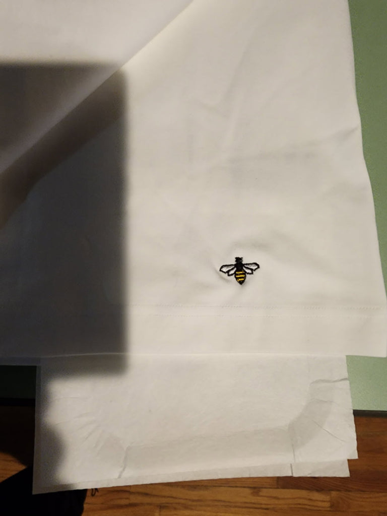Custom embroidered bee logo in black, white, and yellow thread on a white garment, embroidered by Inkdnylon Custom Apparel for a customer.