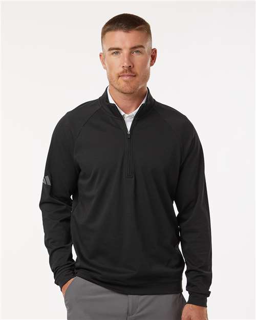 Man wearing a black quarter-zip pullover with raglan sleeves and a small sleeve logo over a white collared shirt.