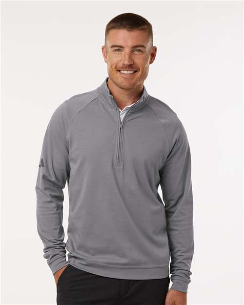 Man wearing a gray quarter-zip pullover with a small sleeve logo and dark pants.