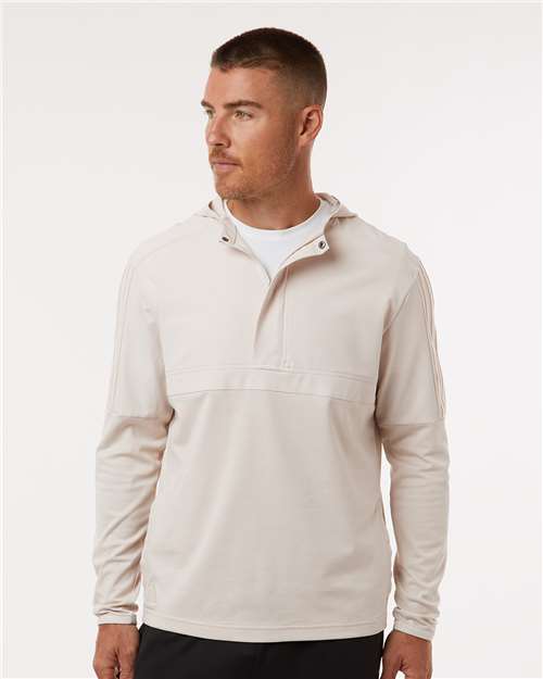 Man wearing a light beige half-zip hooded top with long sleeves and a white undershirt at the neck.