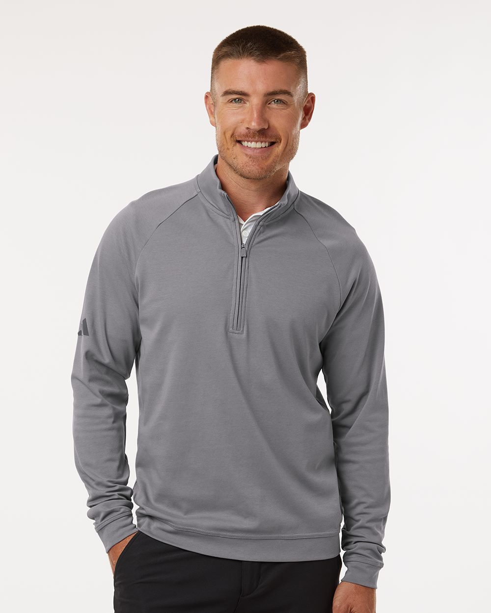 Man wearing a gray quarter-zip pullover with raglan sleeves and a small logo on the upper sleeve.