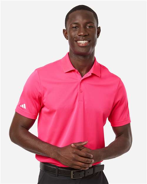 Man in a bright pink short-sleeve polo shirt with a white sleeve logo, dark pants, and a black belt.