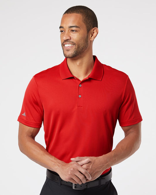 A man wearing a bright red polo shirt with a small silver Adidas logo on the sleeve, paired with black pants and a black belt, photographed against a light gray studio background.