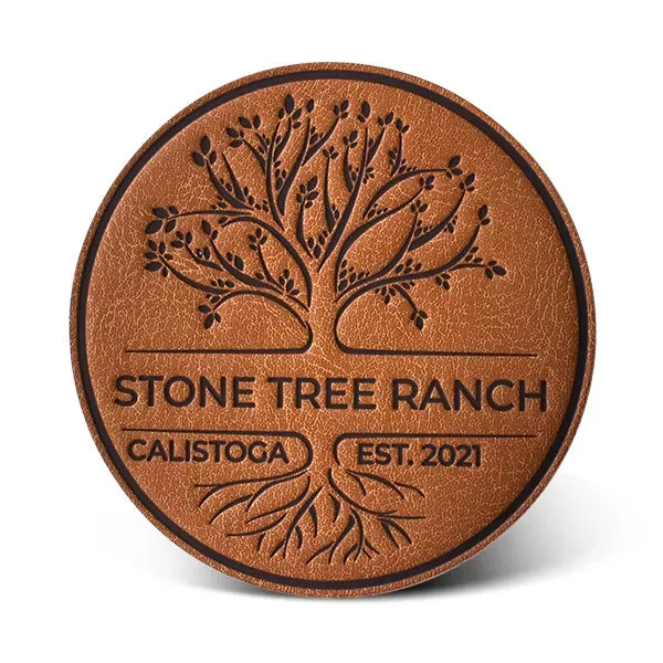 Brown leather coaster with engraved tree design and text on a white background